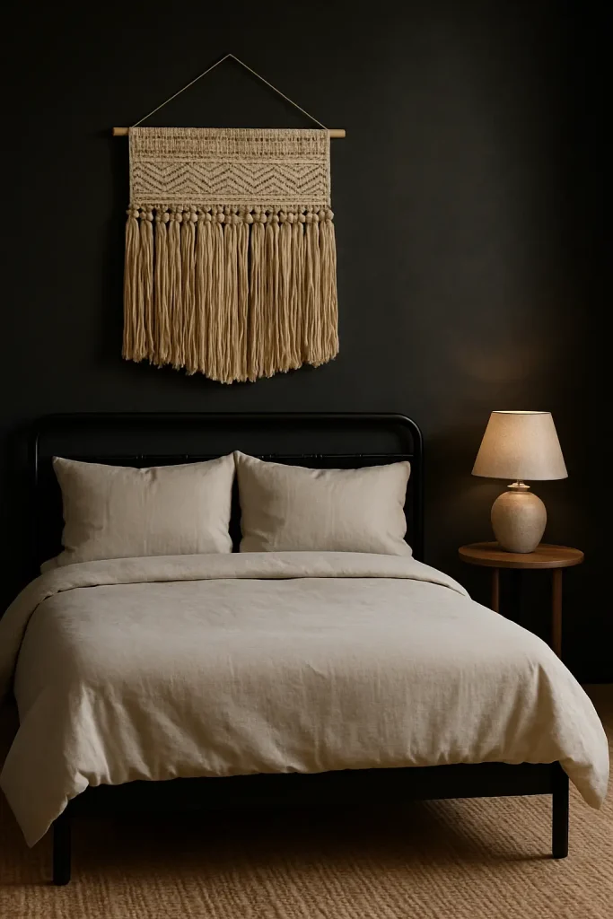 Minimalist dark boho bedroom with black bedframe, neutral sheets, jute rug, and a single woven wall hanging.