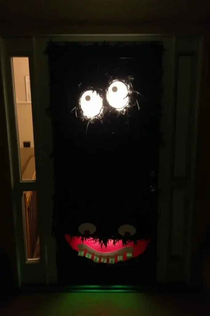 Front door decorated as a glowing monster face with streamers, LED eyes, and yarn fur.