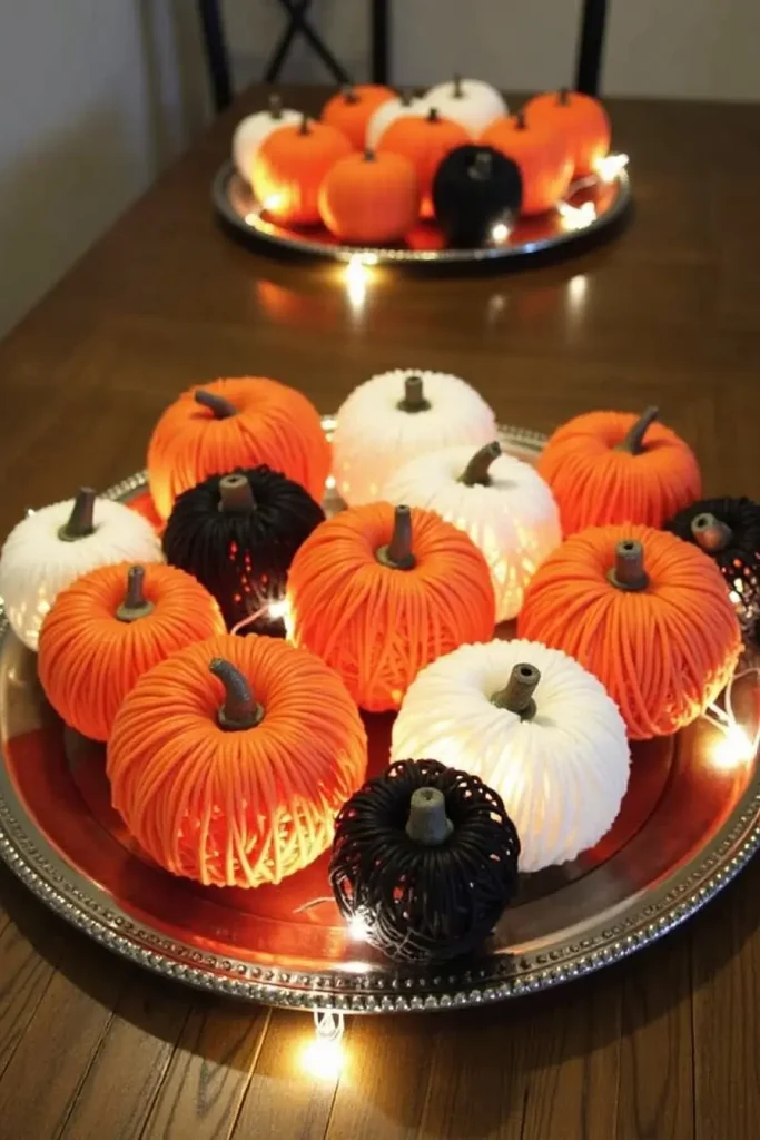 DIY yarn-wrapped pumpkin balls clustered on a tray with fairy lights for a playful Halloween centerpiece.